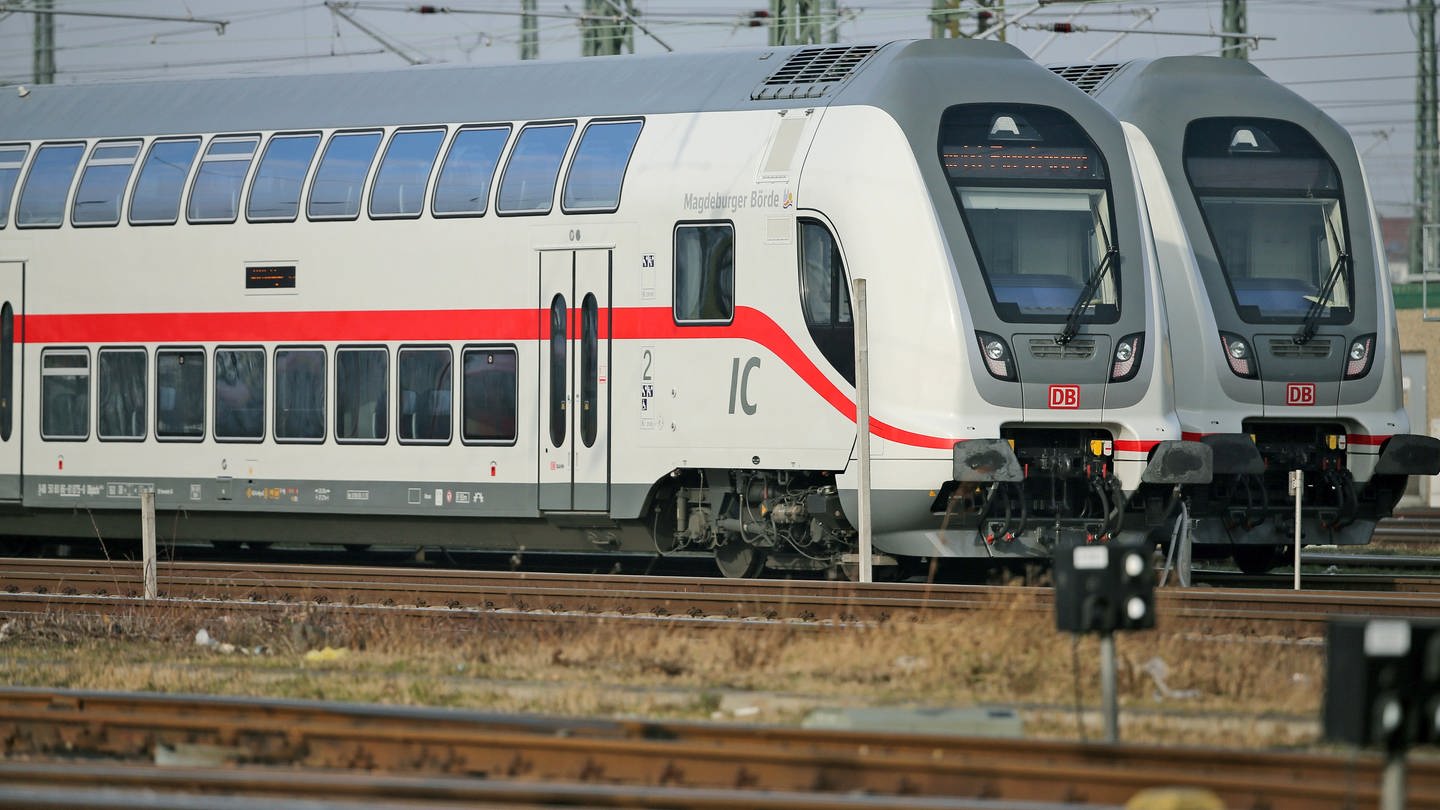 Zwei Doppelstockzüge der zweiten Generation des InterCity stehen auf den Gleisanlagen vor einemHauptbahnhof.