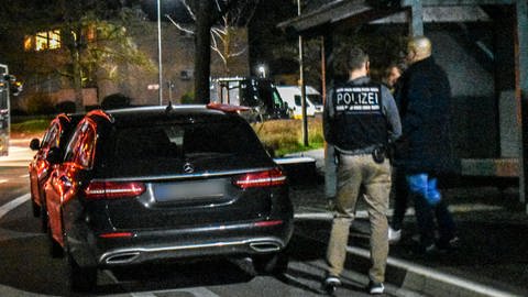 Einsatzkräfte des Kriminaldauerdienstes (KDD) und der Spurensicherung stehen in der Nacht vor dem Tatort. 