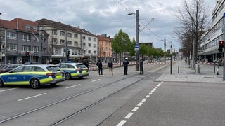 Polizisten bewachen einen mit Polizeiautos und Flatterband abgesperrten Bereich auf der Heilbronner Allee. 