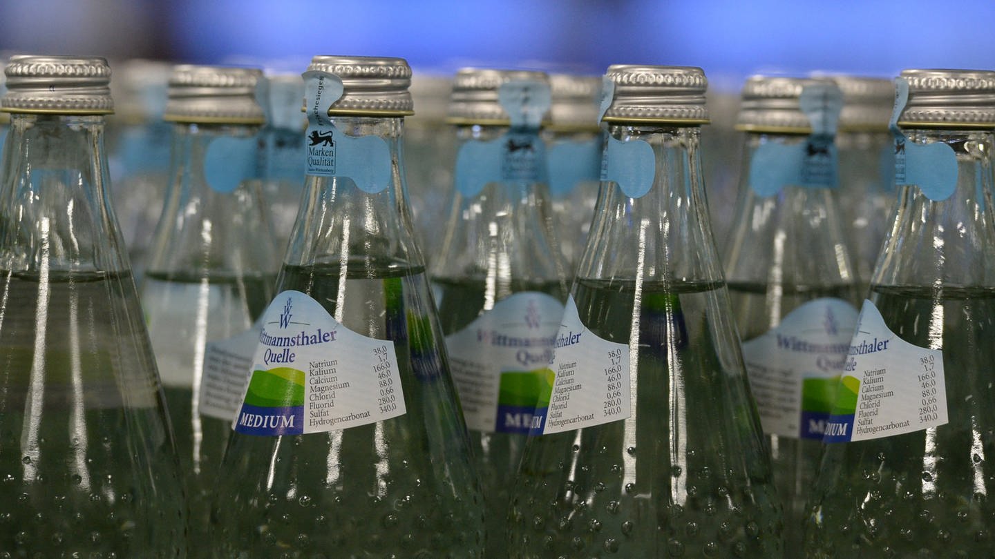 Glasflaschen der Bad Dürrheimer Mineralbrunnen stehen in der Abfüllanlage, man sieht das Etticket und den Flaschenhals.