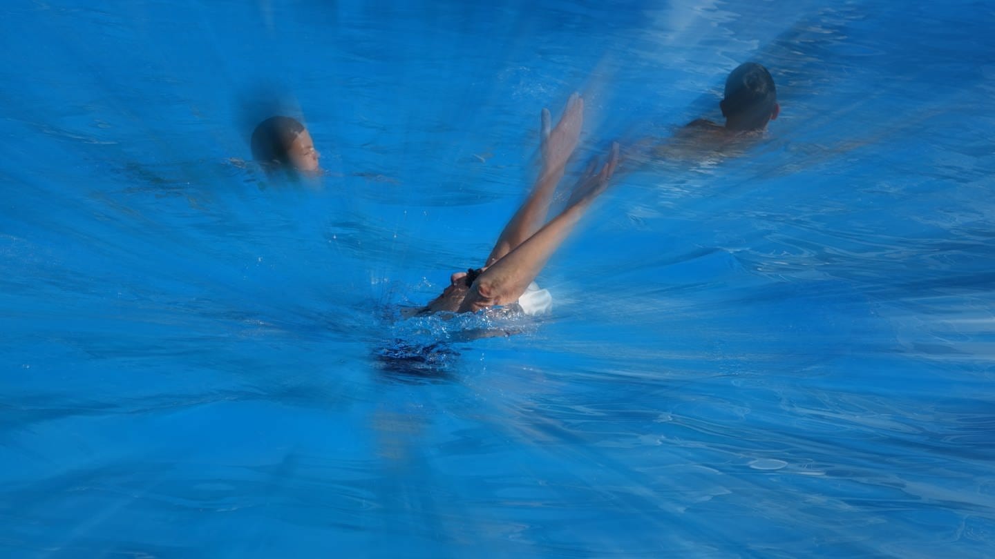 Eine Person im Wasser scheint in Not zu sein. Schwimmende Kinder in der Nähe. Montage Symbolbild Ertrinken.