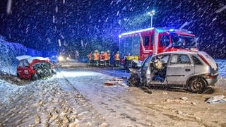 Zwei Unfallwagen stehen auf der Fahrbahn der Bundesstraße B290 bei Blaufelden, im Hintergrund stehen Einsatzfahrzeuge der Feuerwehr und Feuerwehrmänner. Bei einem Frontalzusammenstoß auf schneeglatter Straße ist ein 71 Jahre alter Mann im Landkreis Schwäbisch Hall ums Leben gekommen.