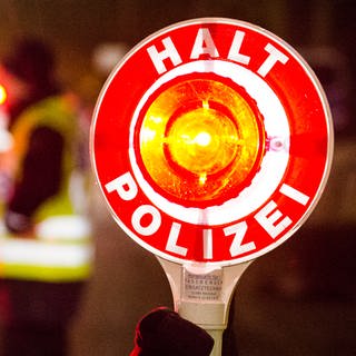  Ein Polizist hält bei einer Verkehrskontrolle eine rote Kelle mit der Aufschrift "Halt Polizei" hoch