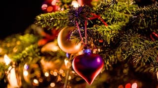 Ein Herzanhänger hängt an einem geschmückten Weihnachtsbaum.