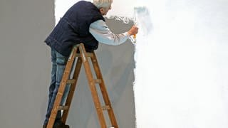 Ein älterer Mann streicht eine Wand (Symbolbild).