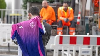 Straßenbauarbeiter beobachten, wie ein Mann mit einem DFB-Trikot entlang läuft