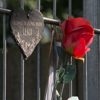 An einem Zaun erinnern ein Herz, eine Rose und eine Kerze an die Verstorbene.