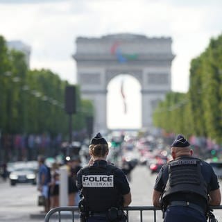 Zwei Polizisten stehen hinter einer Absperrung, im Hintergrund ist der Arc de Triomphe zu erkennen.
