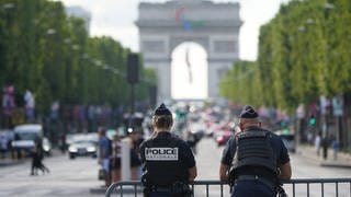 Zwei Polizisten stehen hinter einer Absperrung, im Hintergrund ist der Arc de Triomphe zu erkennen.