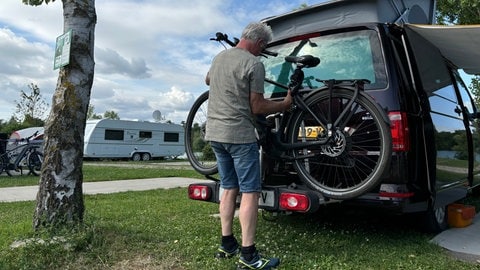 E-Bike-Fahrer befestigt sein Rad auf einem Fahrradträger am Auto.