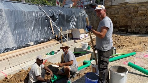 Sajjad Amanat, Hakan Kandemir und Lari Iremir arbeiten in der Sommerhitze auf einer Baustelle.