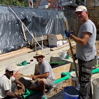 Sajjad Amanat, Hakan Kandemir und Lari Iremir arbeiten in der Sommerhitze auf einer Baustelle.