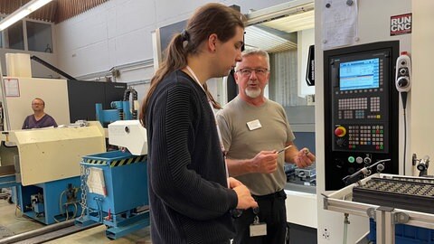 Gruppenleiter Zornik erklärt Manuel Franz eine CNC-Maschine.