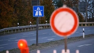 Ein "Durchfahrt verboten" Schild unscharf im Vordergrund, im Hintergrund ein Autobahn-Schild im Fokus.