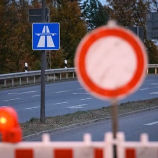 Ein "Durchfahrt verboten" Schild unscharf im Vordergrund, im Hintergrund ein Autobahn-Schild im Fokus.