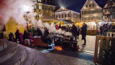 Eine Dampfbahn auf dem Öhringer Weihnachtsmarkt fährt durch das Bild im Hintergrund beleuchtete Buden