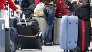 Menschen warten am Flughafen, um sie herum stehen viele Koffer.