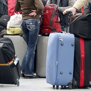 Menschen warten am Flughafen, um sie herum stehen viele Koffer.