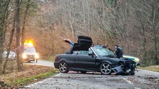 Ein Auto steht nach einem Unfall auf einer Straße. Das Fahrzeug krachte bei Gundelsheim gegen mehrere Bäume und fing anschließend Feuer.