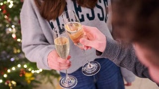 Zwei junge Menschen stoßen mit Sekt vor einem Weihnachtsbaum an