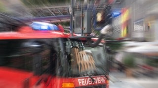 Ein Einsatzfahrzeug der Feuerwehr mit Drehleiter und Blaulicht mit Effekt-Überlagerung Symbolbild