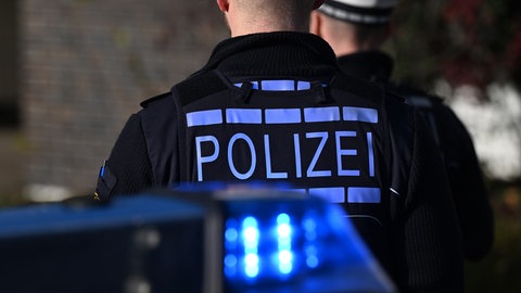 Zwei Polizisten hinter einem Blaulicht eines Polizeiautos (Symbolbild). Nach fünf Überfällen im Kreis Heilbronn sucht die Polizei nach einem möglichen Serientäter.