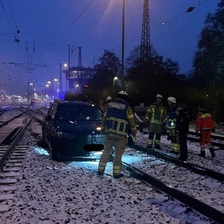 Ein Auto steht auf den Schienen unweit des Heilbronner Hauptbahnhofs. Um das Auto herum stehen mehrere Einsatzkräfte von Feuerwehr, Rettungsdienst und Polizei.