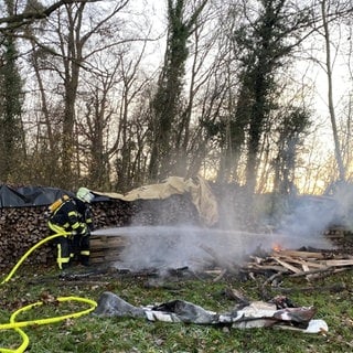 Ein Feuerwehrmann löscht einen brennenden Holzstapel in Eppingen-Mühlbach. Das Feuer ist Teil einer Brandserie - der Brandstifter soll ein Kind sein.