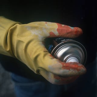 Mann hält Spraydose in der Hand, die in einem Gummihandschuh steckt. 
