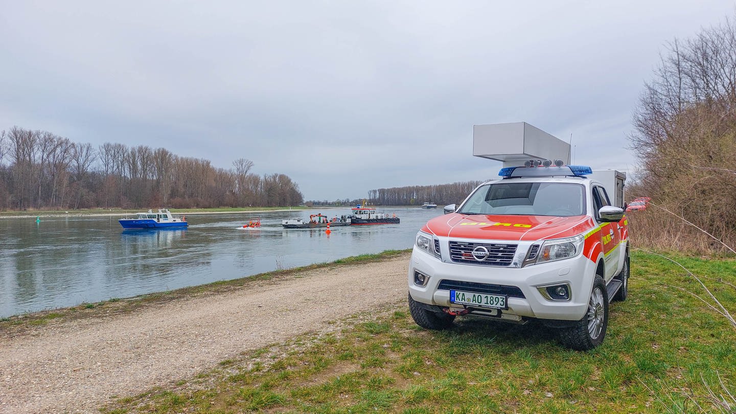 Ein DLRG-Fahrzeug am Rheinufer. Auf dem Fluss sind mehrere Rettungsboote