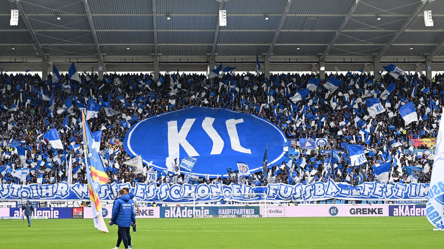 KSC-Fans in der Fankurve im Stadion mit großer KSC-Fahne