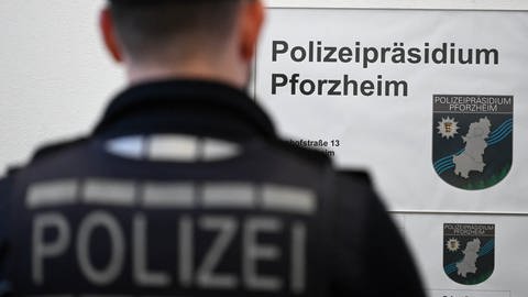 Polizist in Uniform steht mit dem Rücken zum Betrachter neben einem Schild mit der Aufschrift "Polizeipräsidium Pforzheim"