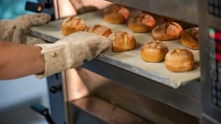 Eine Person schiebt in einer Bäcker-Innung ein Blech mit Brötchen in den Ofen.