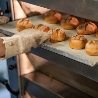 Eine Person schiebt in einer Bäcker-Innung ein Blech mit Brötchen in den Ofen.