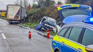 Lkw und Pkw hängen schräg in der Böschung. Davor ein Polizeifahrzeug.