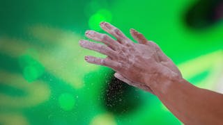 Athletin bestäubt die Hände mit Talkumpuder vor dem Bouldern 