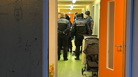 Mehrere Polizeibeamte stehen im Flur eines Wohnhauses, das nach Drogen durchsucht wird.