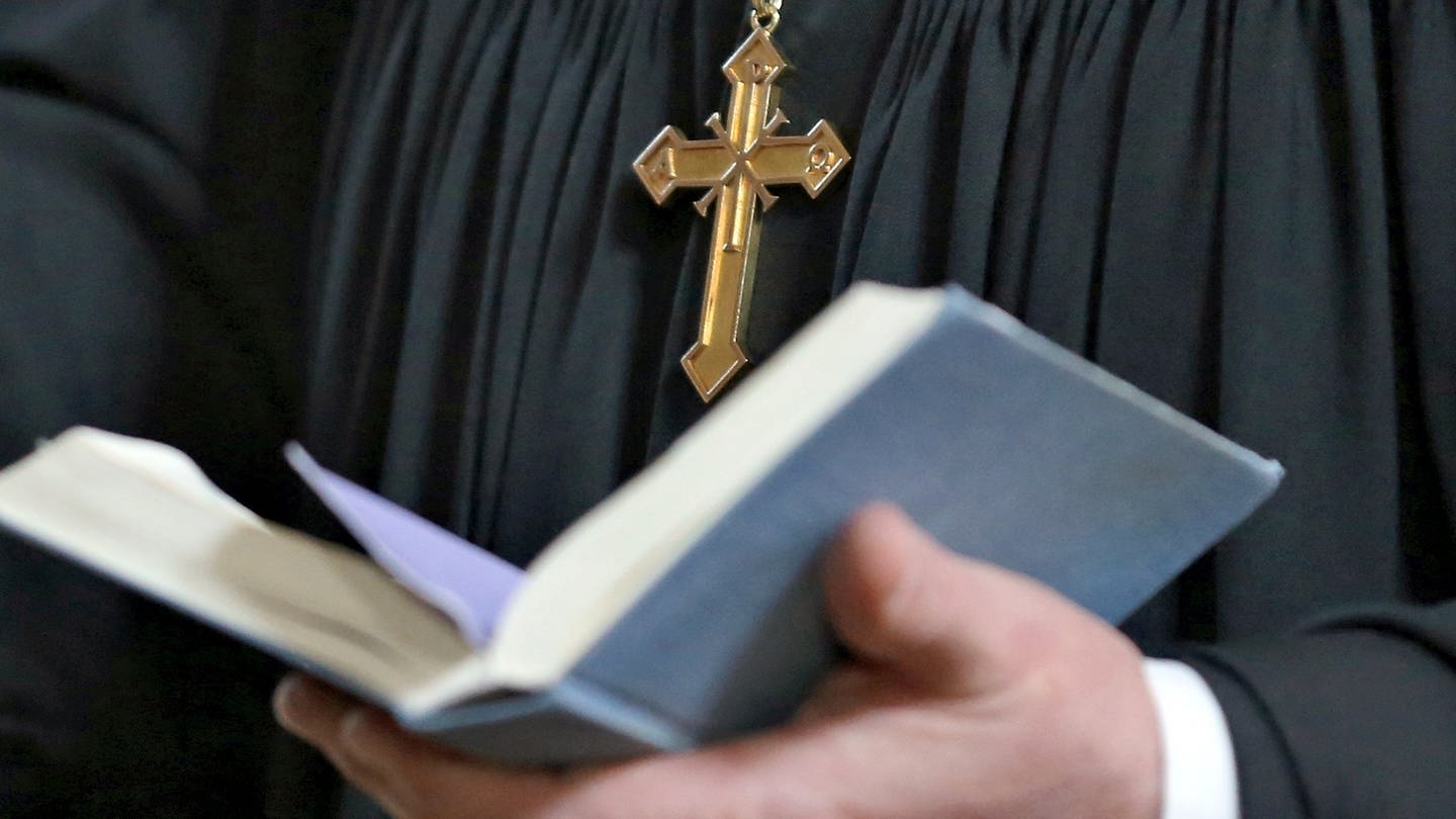 Ein Pfarrer mit einem Kreuz um den Hals und einem Buch in der Hand.