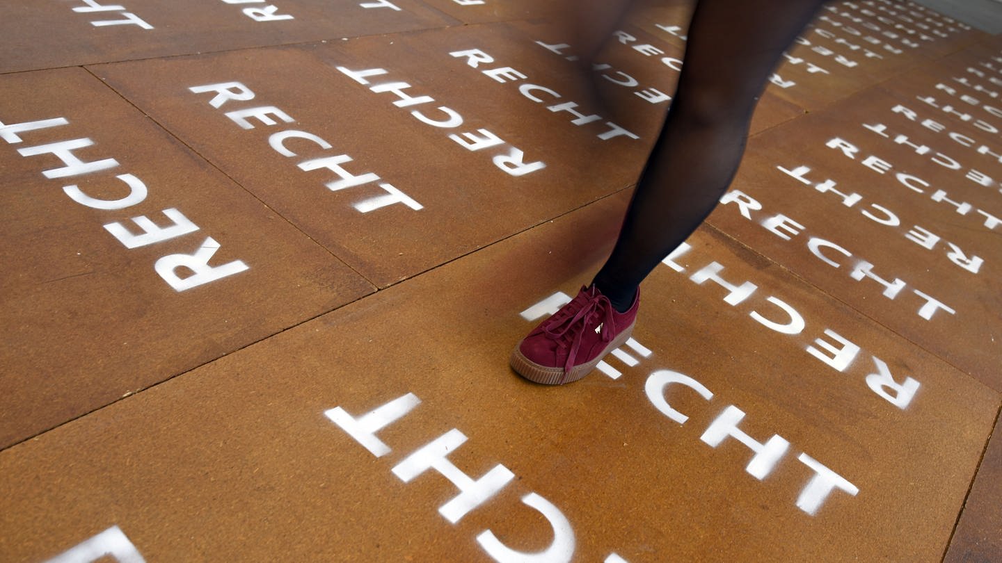 Eine Frau läuft über einen braunen Boden auf dem Recht mehrmals geschrieben steht.