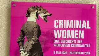 Plakat zur Ausstellung "Criminal Women" im LA8 in Baden-Baden. Es zeigt auf magentafarbenem Grund eine Frau in einem Kostüm der Jahrhundertwende mit einem Wolfskopf