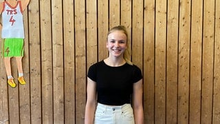 Anna-Lena König, Schülerin der Tulla-Realschule in Karlsruhe, steht in der Sporthalle vor einer hölzernen Wand.