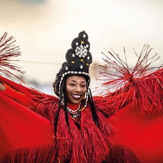 Singer-Songwriterin und Rock-Gitarristin Fatoumata Diawara. Sie trägt ein knall-rotes Kleid und breitet die Arme aus. Sie tritt beim ZELTIVAL im Tollhaus Karlsruhe auf.