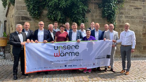 Vertreter von Städten und Kommunen im Landkreis Karlsruhe halten ein Transparent mit der Aufschrift: "Unsere Wärme - Nahhaltig aus dem Oberrheingraben".