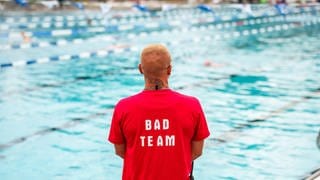 Symbolbild Sicherheitspersonal im Freibad. Mann im roten T-Shirt überwacht Schwimmbecken.