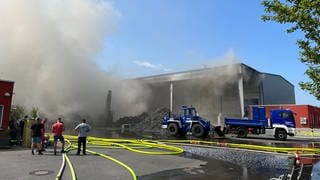 Feuerwehrleute löschen einen Großbrand auf einem Recyclinghof in Oberderdingen. Über der Lagerhalle steht eine große Rauchwolke.