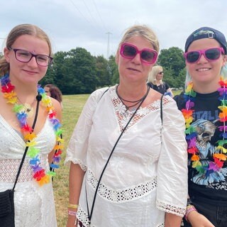 Drei Besucherinnen des Happiness-Festivals in Straubenhardt tragen pinke Sonnenbrillen und bunte Blumenketten