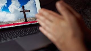 Symbolbild: Auf einem Computerbildschirm ist ein Kreuz zu sehen, davor Hände
