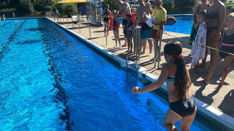 Schwimmkurs für Kinder im Wartbergbad in Pforzheim - ein Mädchen springt ins Becken, Badegäste schauen vom Beckenrand zu