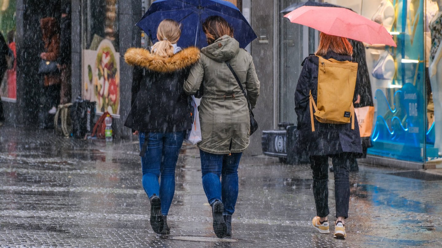 Der nasseste November in der Wettergeschichte: Drei Personen laufen mit Regenschirm durch den Regen