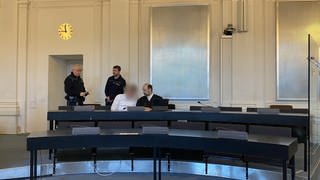 Der tatverdächtige Ehemann sitzt auf der Anklagebank am Landgericht Karlsruhe. Neben ihm sein Verteidiger und im Hintergrund sind zwei Justizbeamten zu sehen. Die Staatsanwaltschaft fordert eine lebenslange Gefängsnisstrage für den Angeklagten. Am Freitag soll das Urteil fallen.